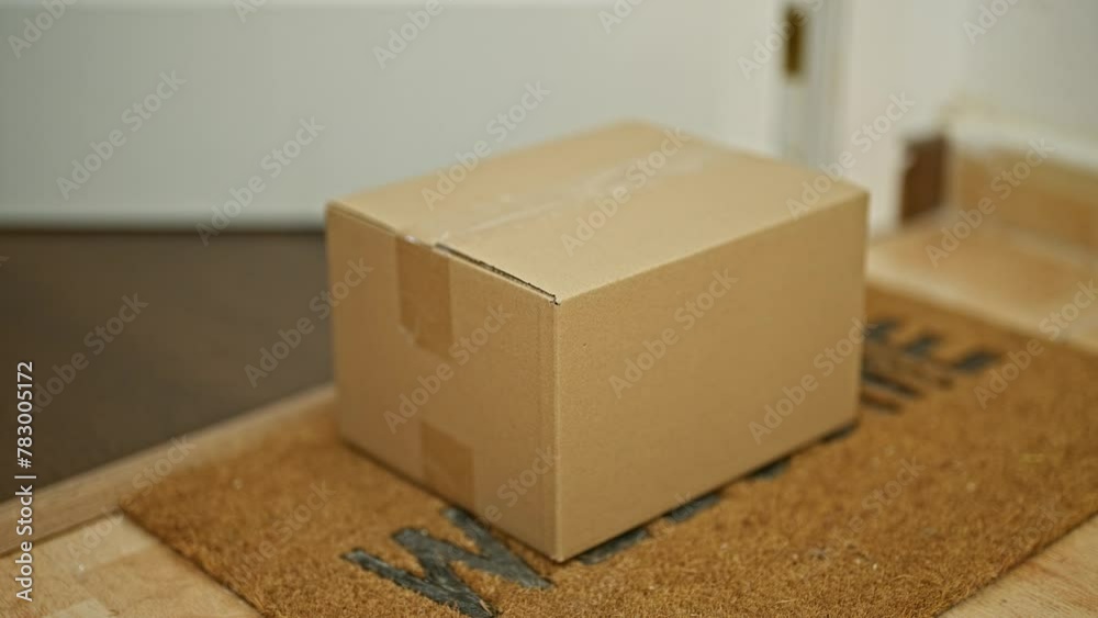 Cardboard package delivery at the doorstep inside a house with a welcome mat and red sneakers