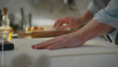 Confectioner. A modern chef dressed in a uniform professionally shapes a sheet of dough in the kitchen. Mature man working with dough rolling pin follows sustainable business trends, dessert photo