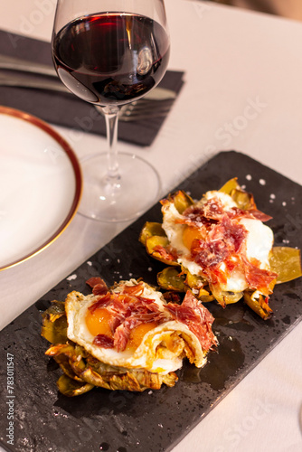 Plato en mesa con vino tinto, alcachofas, huevos y jamón en restaurante 