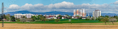Satellitenstadt am Rand von Frankfurt am Main mit Feldern, Streuobstwiese und dem Mittelgebirge Taunus im Hintergrund bei sonnigen Wetter und aufgelockerter Bewölkung