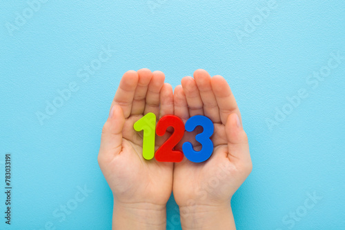 Baby boy hands holding and showing colorful 123 numbers on light blue table background. Pastel color. Time to learning. Closeup. Point of view shot. Top down view.