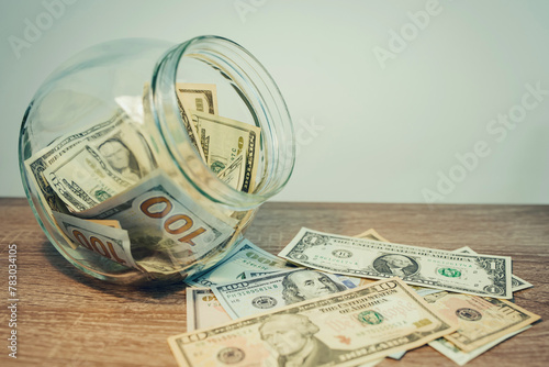 Close up of transparent money box with dollar banknotes inside and nearby on the table. Toned picture with concept of richness, wealth, savings and prosperity © Vitalii