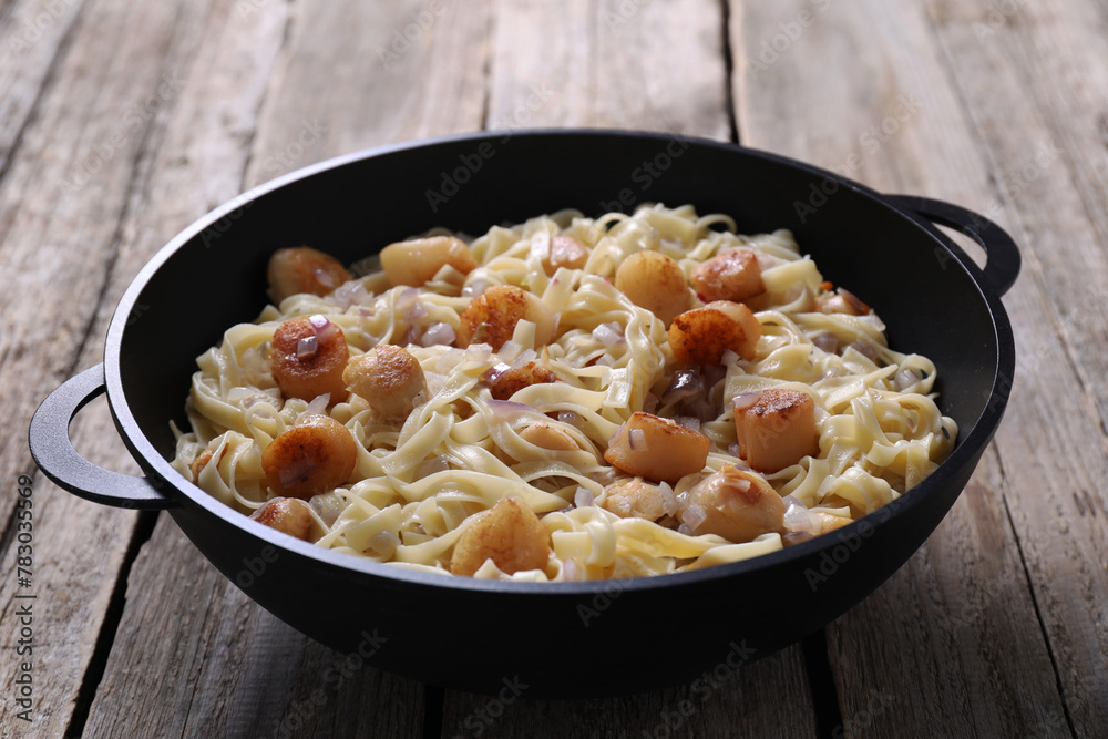 Delicious scallop pasta with onion in pan on wooden table, closeup Delicious scallop pasta with onion in pan on wooden table, closeup