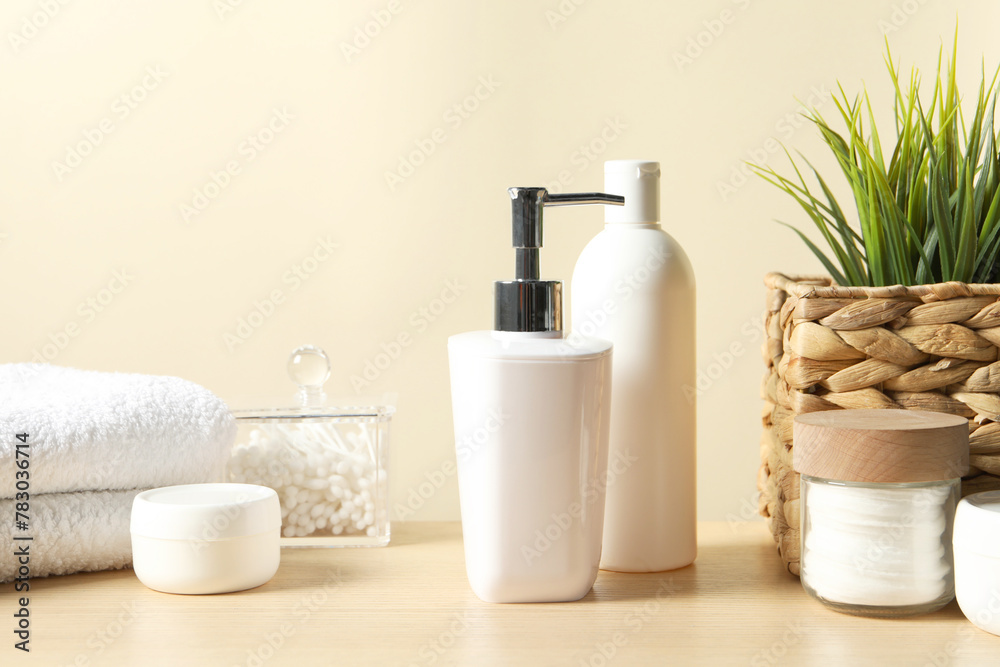 Different bath accessories and houseplant on wooden table against beige background, closeup