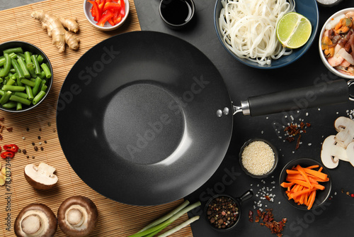 Flat lay composition with black wok, spices and products on dark table