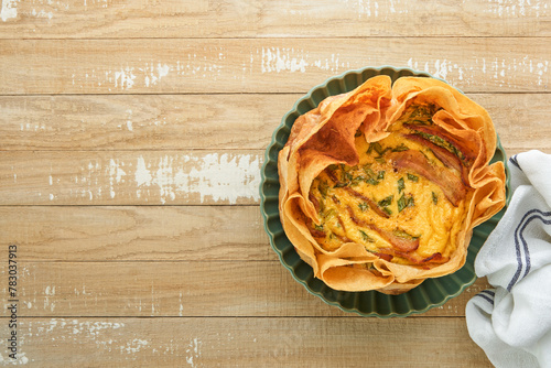 Homemade quiche or tart with slices of bacon and leeks with tortilla instead of dough on wooden cutting board on rustic old wooden background. Quiche open tart traditional French cuisine. Top view.