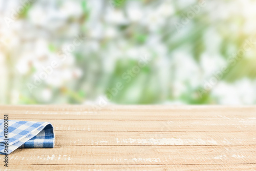 Empty rustic wooden table with blue tablecloth over blooming summer garden on sunny day background. Harvest mock up for design.