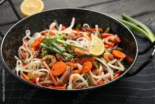 Shrimp stir fry with noodles and vegetables in wok on black wooden table, closeup