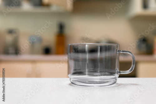 Empty glass cup sitting on laminated kitchen benchtop, Cupboards and cooking appliances in background.