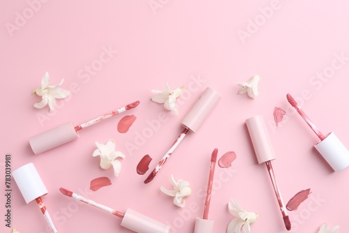 Different lip glosses, applicators and flowers on pink background, flat lay. Space for text