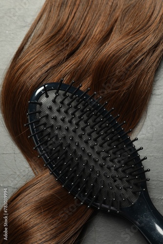 Stylish brush with brown hair strand on dark grey table, top view