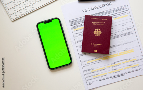 Top view of a visa application document with a German passport and a smart phone with green screen