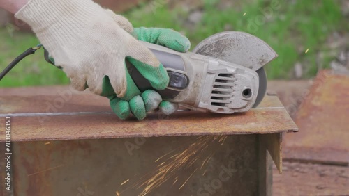 An old angle grinder cuts rusty metal along the intended line. The hands of a worker in green protective gloves