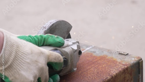 An angle grinder cuts old rusty metal, the worker's hands are gloved. Close-up