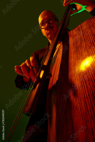 Photography Artistic, talented young bass player performing jazz composition in red-green neon light against gradient studio background