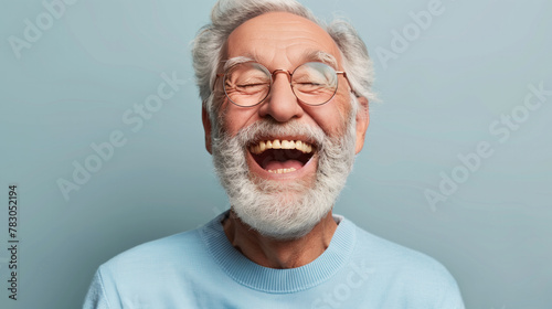 A man with a big smile on his face is wearing glasses and a blue shirt. He is laughing and he is happy. laughing old man, beard, glasses, happy, open laugh, enthusiastic, light blue sweater