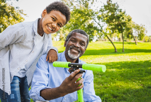 Beautiful happy african american family bonding at the park- Black grandfather teaching his grandson how to ride on scooter photo