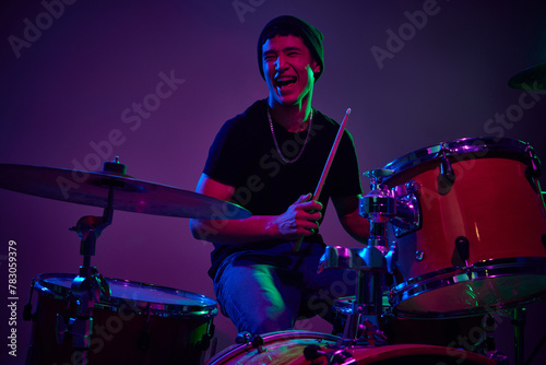 Joyful contemporary drummer playing in pink-purple stage lighting against gradient studio background. Concept of music and art, hobby, concerts and festivals, modern culture. Ad