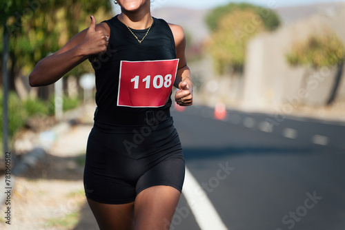 Marathon runner woman gesturing thumbs up outdoors in a city outskirts