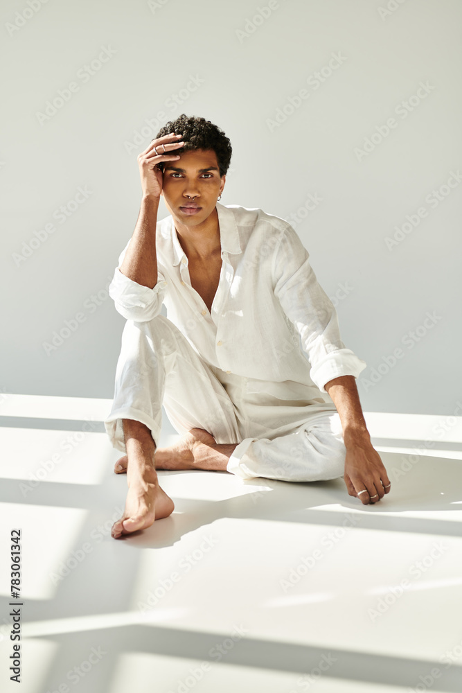 exquisite young african american man in linen attire looking at camera on floor on beige backdrop exquisite young african american man in linen attire looking at camera on floor on beige backdrop