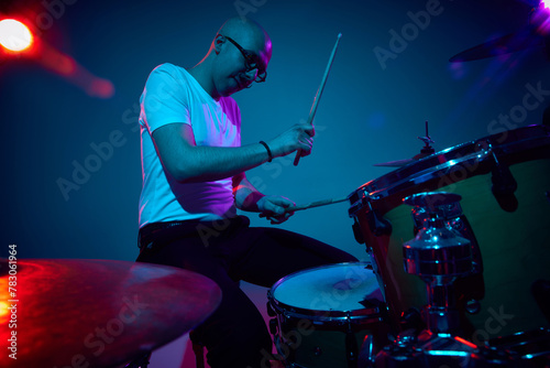 Focused bald drummer in white shirt playing in pink-purple stage lighting against gradient studio background. Concept of music and art, hobby, concerts and festivals, modern culture. Ad