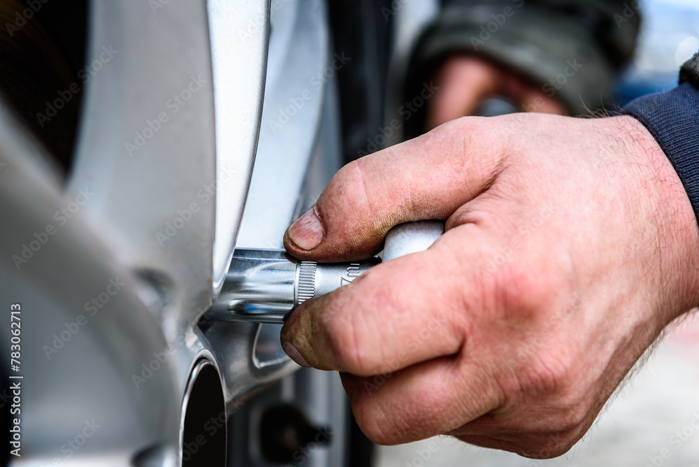 Auto mechanic with a torque wrench changing tires on wheels outside.