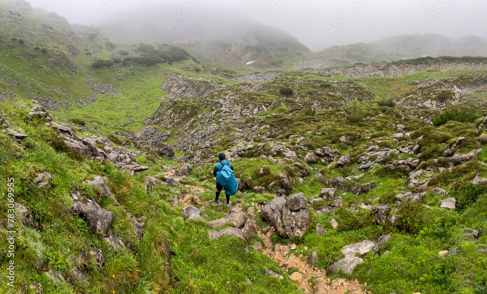 Fototapeta premium Man hike alone though the Bavarian mountains and he use a trash bag as his rain water protection