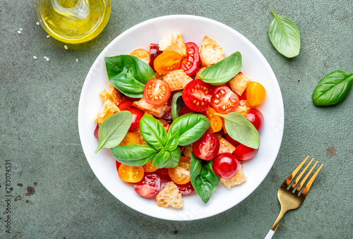 Simple italian salad with with stale bread, cherry tomatoes, olive oil, sea salt and green basil white plate, stone table background, top view