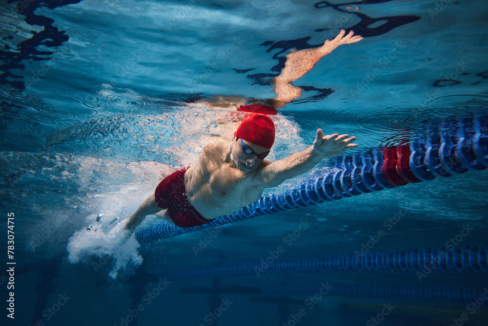 Powerful strokes. Freestyle swimming type. Young man, swimmer in motion training in swimming pool. Concept of professional sport, health, endurance, strength, active lifestyle