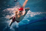 Resilience and strength. Concentrated young man in red cap and goggles in motion, swimming in pool, training. Concept of professional sport, health, endurance, strength, active lifestyle