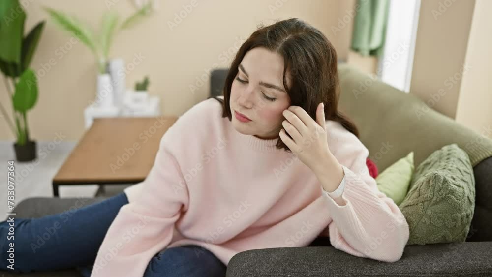 A thoughtful woman sits on a sofa in her cozy living room, embodying relaxation and comfort. A thoughtful woman sits on a sofa in her cozy living room, embodying relaxation and comfort.