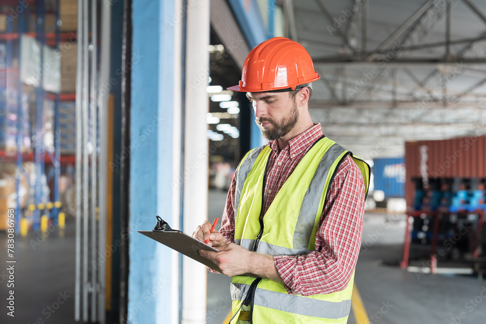 Obraz premium Male warehouse worker holding clipboard during working in storage warehouse. Warehouse worker inspecting quality of products and checking stock inventory