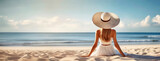 Young woman sits on sandy beach in sun hat and looks on endless ocean waves in distance. Rear view of slender beautiful girl resting by the sea. Panorama with copy space.