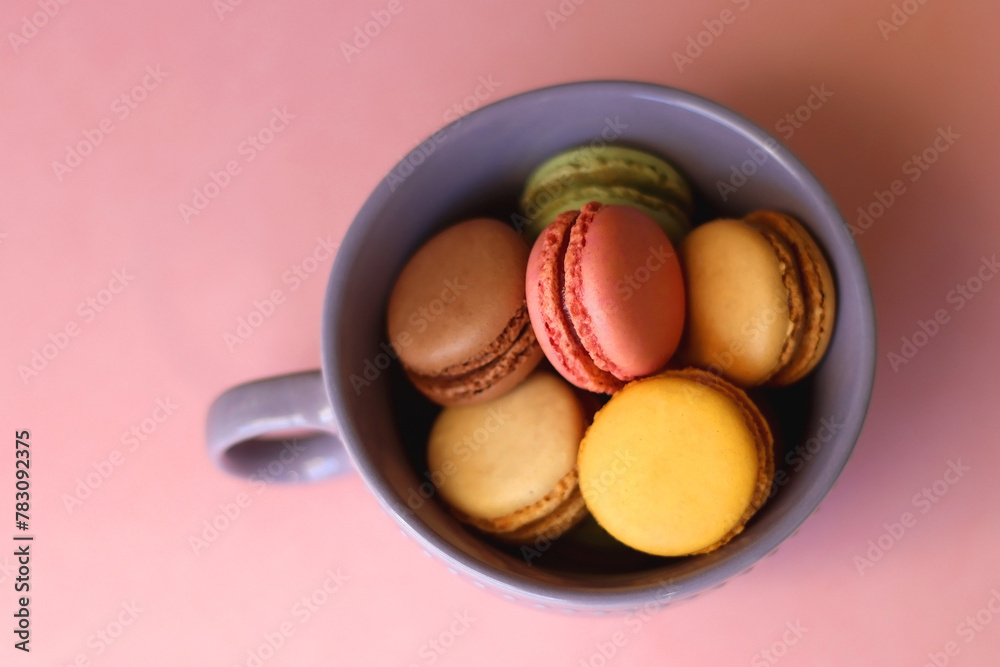 Purple cup filled with pastel macarons on pink background. Selective focus. Purple cup filled with pastel macarons on pink background. Selective focus.