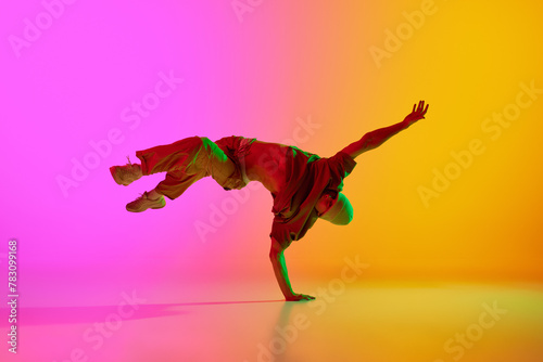 Talented young man dancing in hip-hop style, performing in neon light against gradient pink-yellow background. Concept of art, hobby, sport, creativity, fashion and style, action. Ad