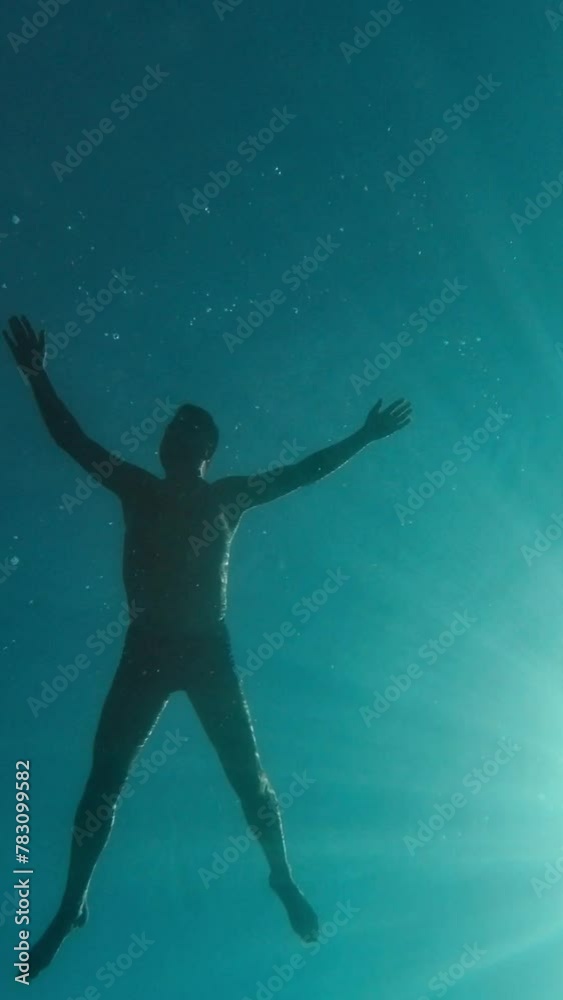 Underwater shot. A man is floating on the surface of the water against the background of the sky and the sun, looking at the seabed and fish Vertical Video Underwater shot. A man is floating on the surface of the water against the background of the sky and the sun, looking at the seabed and fish Vertical Video