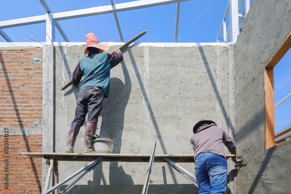 2 Asian builder workers on wooden scaffolding are plastering and polishing concrete wall room in house construction site