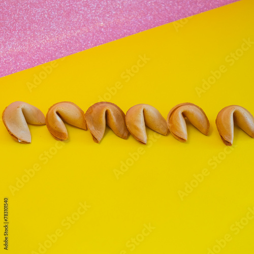 A fortune cookies are laid out in a line on yellow and pink backgrounds, creative concept
