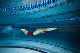 Butterfly swim style. Athletic young man, swimmer in motion training, preparing for competition, swimming in pool indoors. Concept of professional sport, health, endurance, strength, active lifestyle