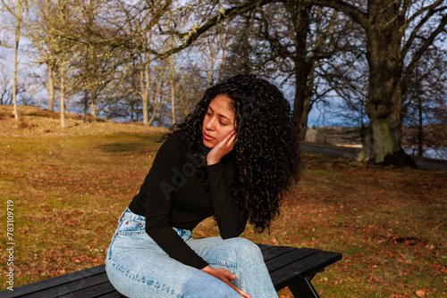 Model shoot in a park of a curly-haired Latina girl with a thoughtful face sitting on a bench