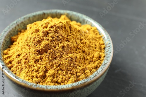 Dry curry powder in bowl on dark table, closeup