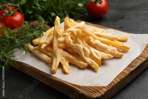 Delicious French fries with cheese sauce, tomatoes and dill on black table, closeup