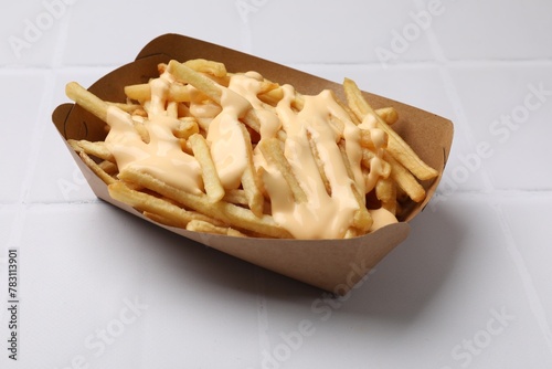 Obraz na plátně Delicious French fries with cheese sauce on white tiled table, closeup