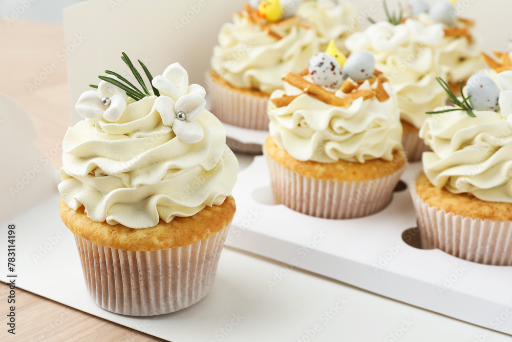 Tasty Easter cupcakes in box on wooden table, closeup
