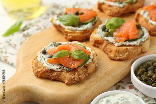 Tasty canapes with salmon, capers, cucumber and sauce on table, closeup