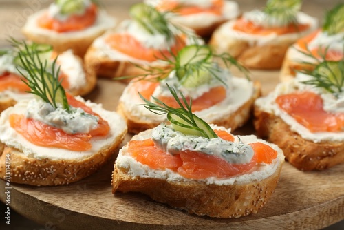Tasty canapes with salmon, cucumber, cream cheese and dill on wooden stand, closeup
