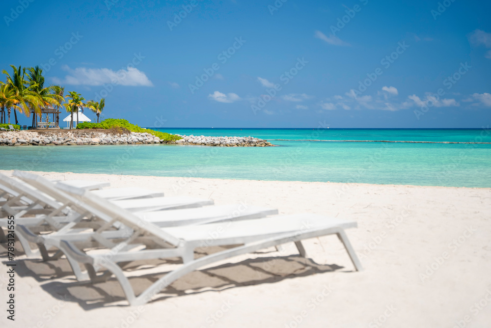 The row of empty sun loungers on a beautiful tropical beach with white sand and turquoise sea water without people. The best summer vacations ideas and destinations. Caribbean copy space background 
