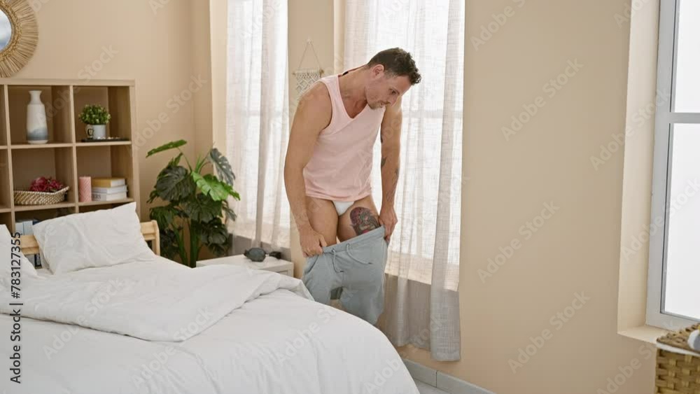A young man with a beard getting dressed in a modern bedroom setting, talking on the phone A young man with a beard getting dressed in a modern bedroom setting, talking on the phone