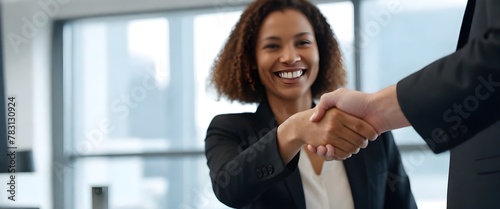 Close-up of a handshake in focus with a smiling woman in a black blazer in the background