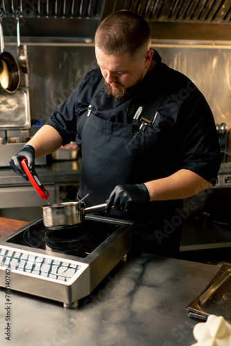 in a professional kitchen chef in a black jacket measures the temperature of the sauce in a saucepan